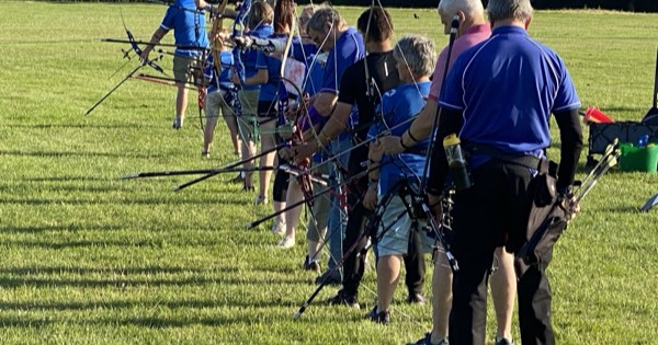 A row of recurve archers standing side by side on the shooting line at an outdoor club range