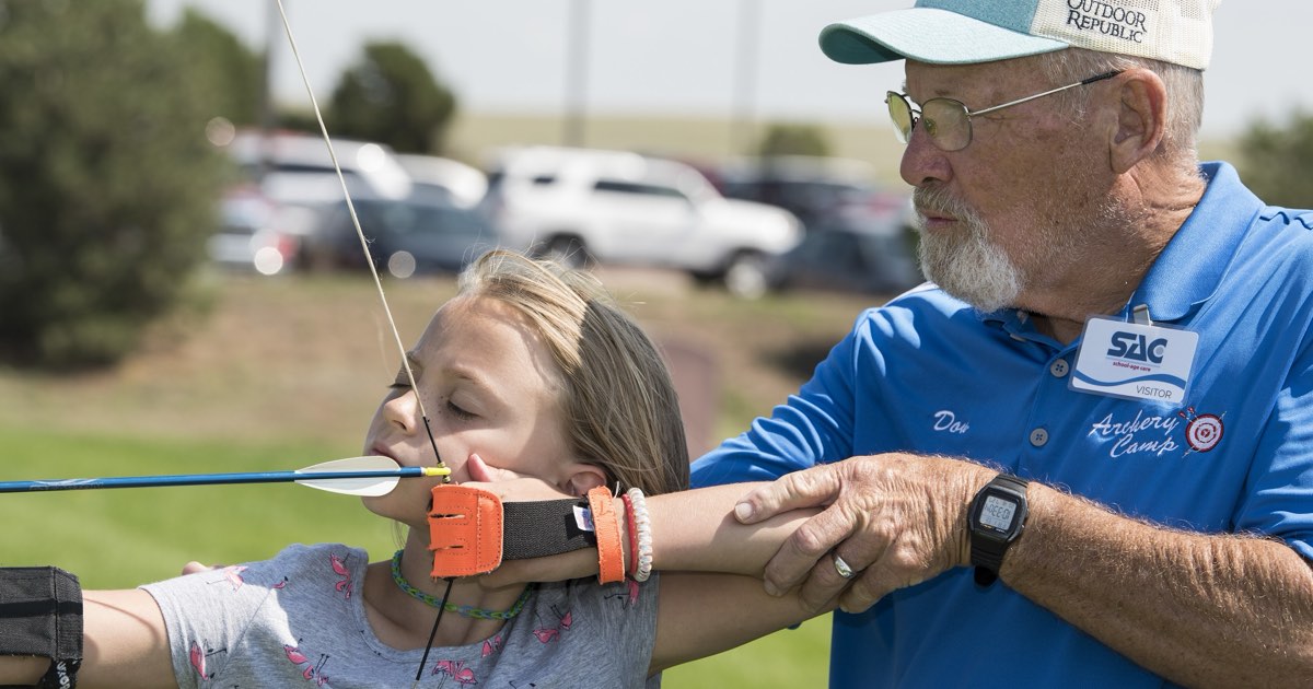 A coach adjusting a girl's anchor and bow arm as she draws a youth recurve