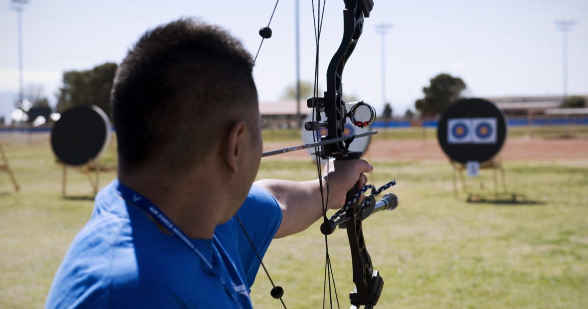 Archer aiming a compound bow at outdoor targets under a clear sky