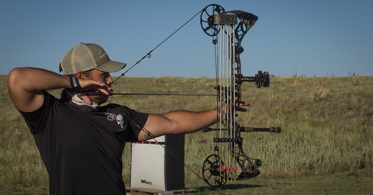 Compound archer at full draw on an outdoor range, with a sight and stabilizer fitted to the bow