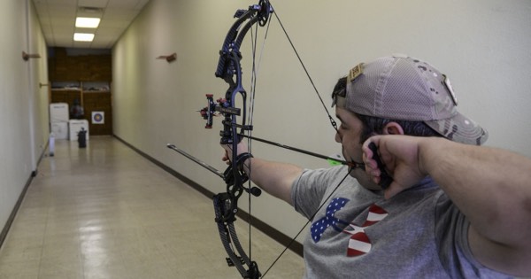 Archer drawing a compound bow on an indoor range with a target at the far end