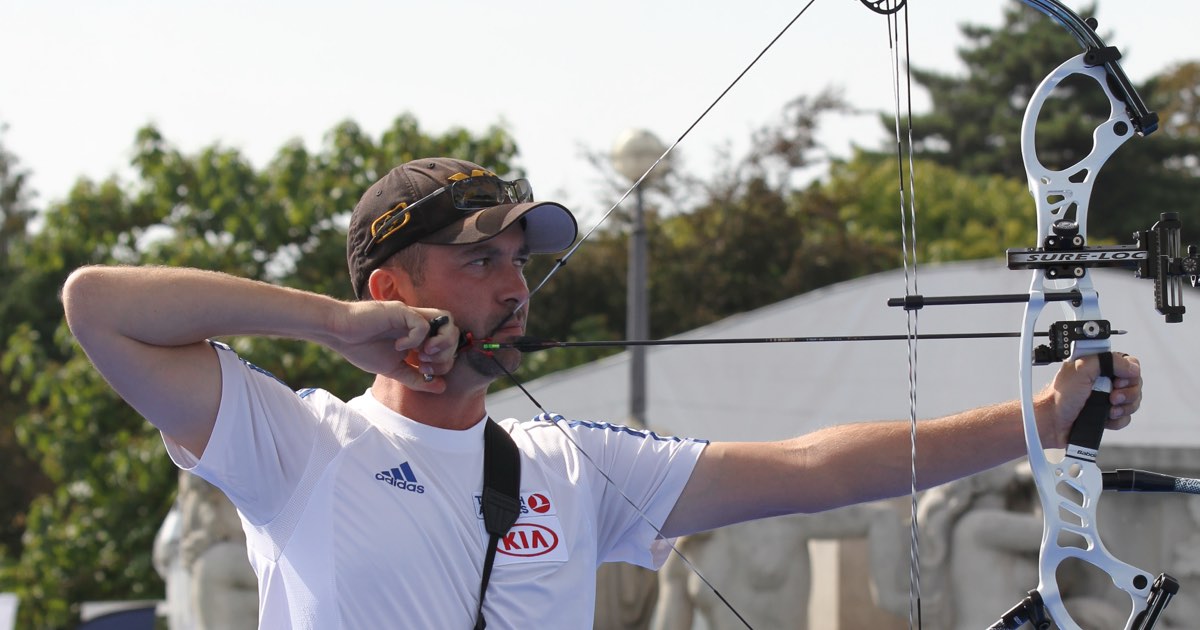 Compound archer at full draw with a white target compound bow at an outdoor competition