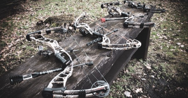 Several modern compound bows laid out on a wooden table
