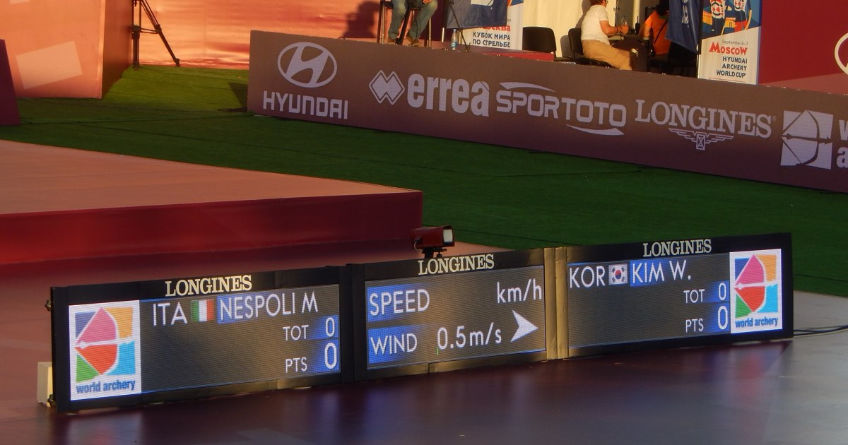Compound archers at the shooting line in front of Archery World Cup branding at the 2019 Final in Moscow