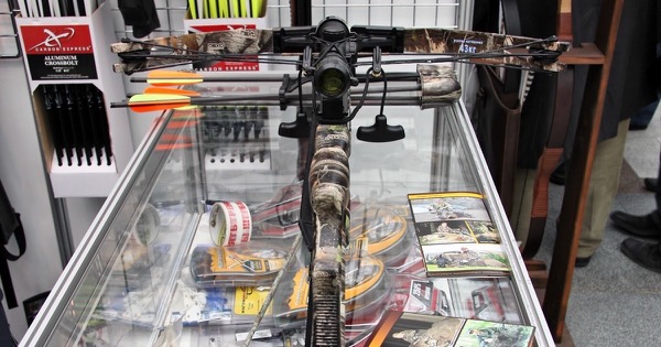 Front view of a camouflage compound crossbow on a shop counter, with the draw weight printed on its limbs