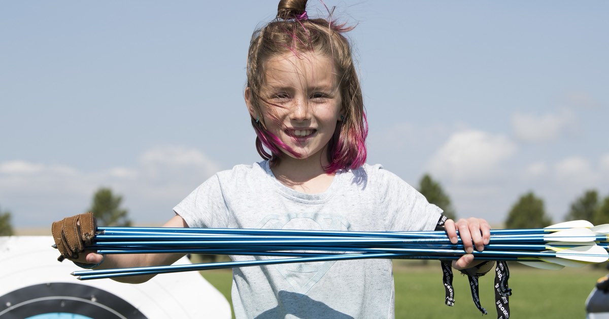 A smiling girl holding a handful of arrows she has just collected from the target