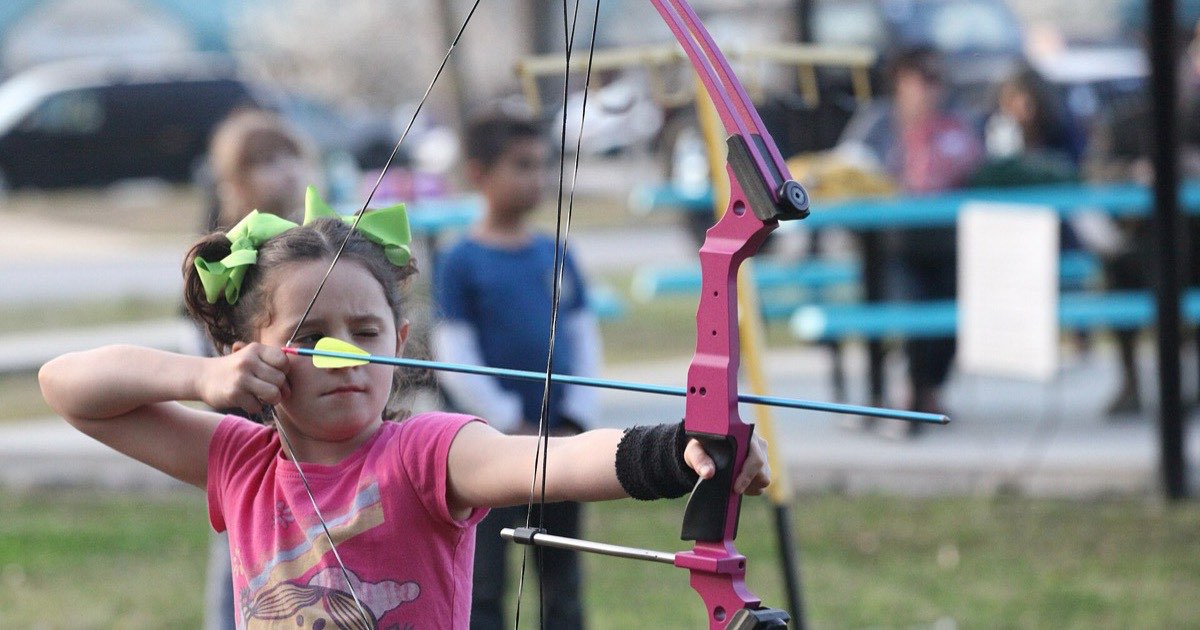 Young girl at full draw with a pink youth bow and arm guard at an after-school archery programme