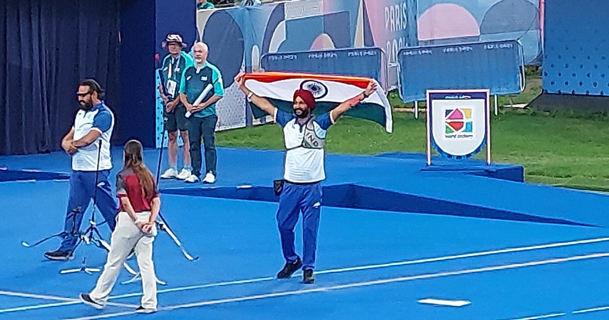 Harvinder Singh of India holding the Indian flag aloft on the field at the Paris 2024 Paralympic archery venue