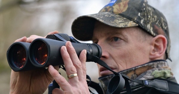 Hunter in a camouflage cap looking through binoculars