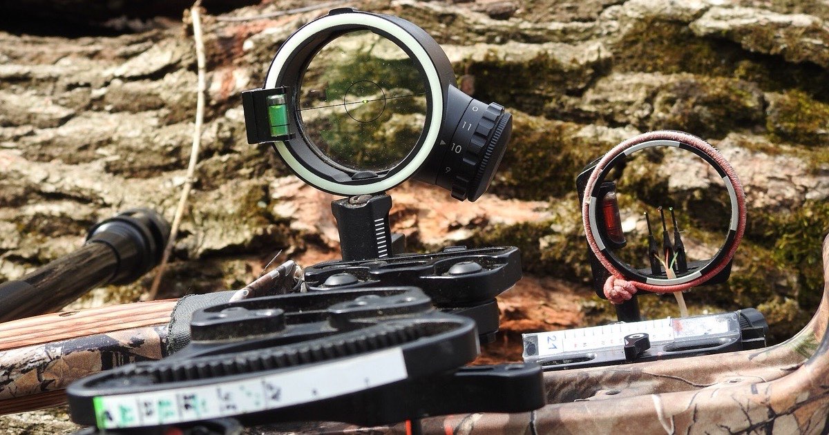 A single-pin and a multi-pin hunting bow sight resting on a log