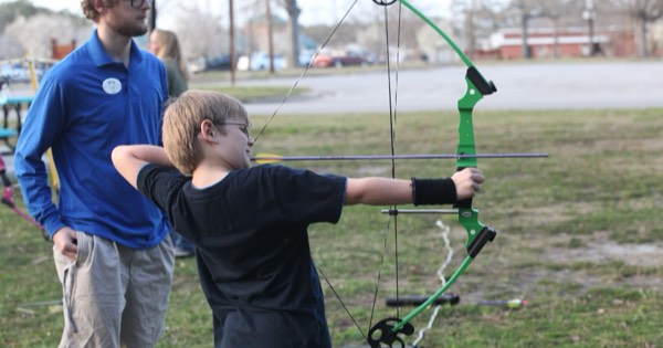 Young archer drawing a green youth compound bow with a coach watching at an after-school programme