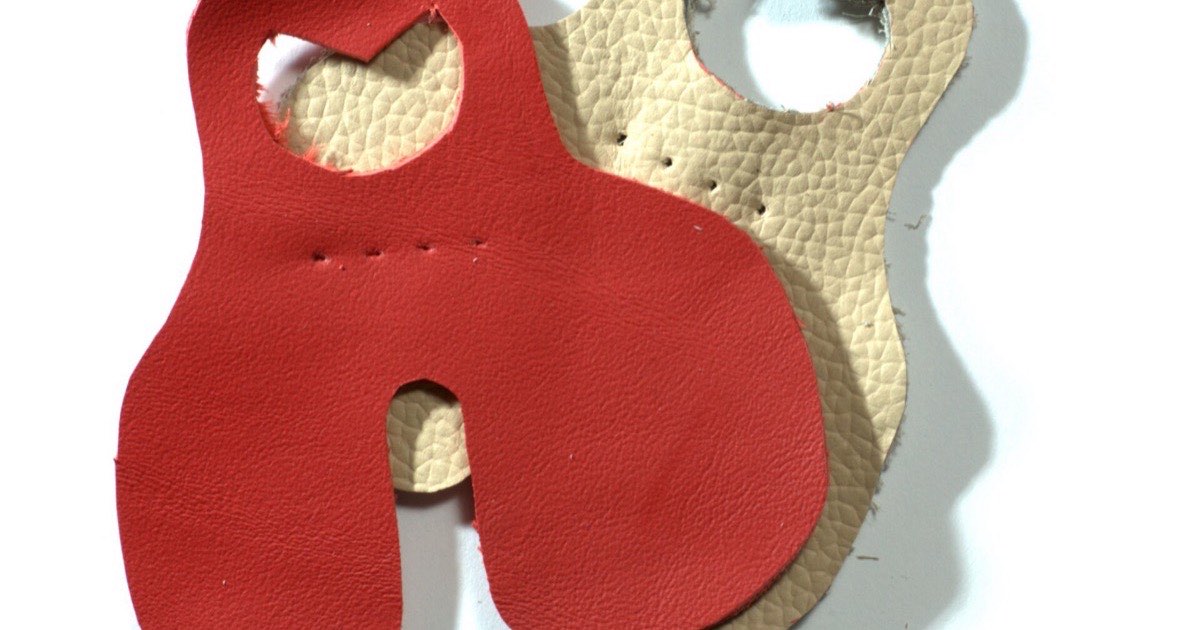 Two leather finger tabs, one red and one cream, each cut with finger holes