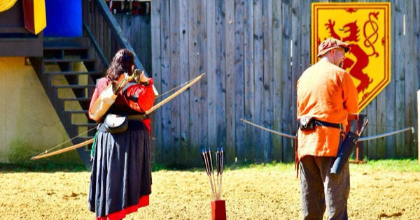 Two traditional archers with longbows and arrows at the shooting line