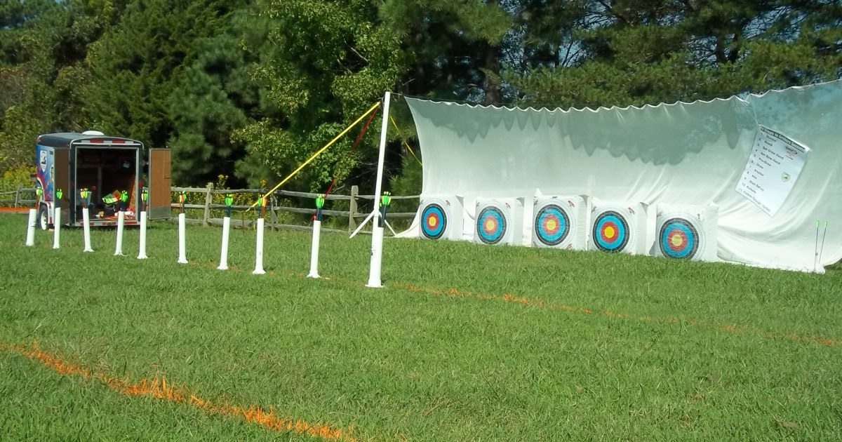 An outdoor archery range with a line of target bosses in front of a tall white safety net