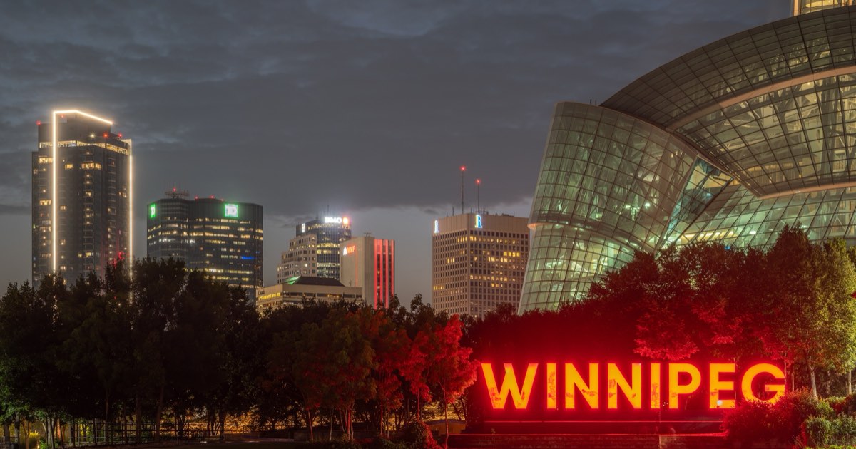 Illuminated WINNIPEG sign at The Forks with the downtown skyline and Canadian Museum for Human Rights at dusk